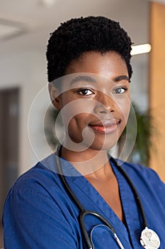 Vertical portrait of smiling african american female doctor in hospital corridor