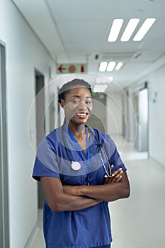 Vertical portrait of smiling african american female doctor in hospital corridor, copy space