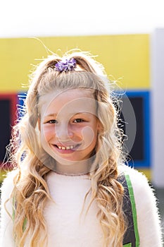Vertical portrait of smiling cauasian elementary schoolgirl in school playground, copy space photo