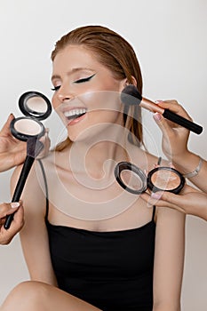 Vertical portrait of smiling, elegant, fashionable woman and cropped visagiste hands apply make up with powder and brush