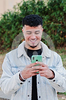 Vertical portrait of smiling moroccan guy having fun using a smartphone to play a video game. Happy teenager texting
