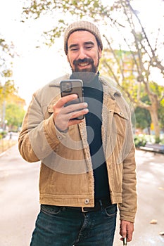 Vertical portrait smiling young man is browsing the internet with a smartphone outdoors.