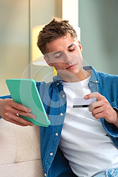 Vertical portrait Smiling Young man shopping online with credit card and a tablet indoor
