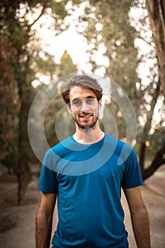 Vertical portrait of smiling young man standing in the forest looking at camera.