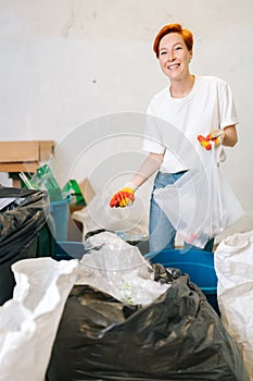 Vertical portrait of smiling young woman worker wearing latex gloves sorting diverse waste for further disposal at