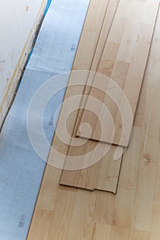 A vertical portrait of a stacked pile of wood imitation laminate floorboards lying on some sound isolation ready to be installed