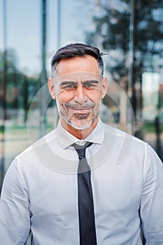 Vertical portrait of successful mature caucasian business man smiling looking at camera standing outdoors at workplace