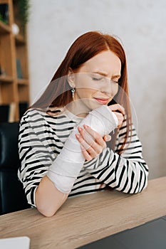 Vertical portrait of suffering from pain crying young woman with broken right hand wrapped in gypsum bandage sitting at