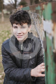 Vertical portrait of a teenager near an iron fence. The boy smiles and the braces are visible on his teeth