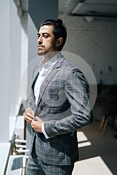 Vertical portrait of thoughtful stylish business man wearing fashion suit standing in modern office room, looking out