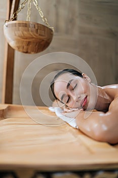 Vertical portrait of tranquil young woman lying on massage table with closed eyes enjoying leisure in wellness center