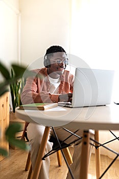 Vertical portrait of young African American man wearing headphones working, studying at home using laptop. Copy space.