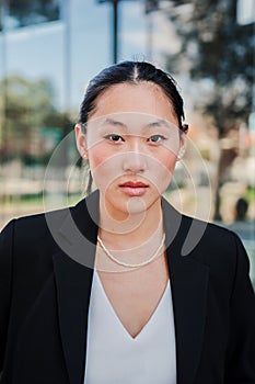 Vertical portrait of young asian business woman or executive looking serious at camera wearing a suit standing at