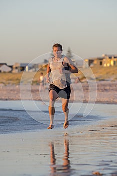Vertical portrait of young athletic fit and strong runner man training on Summer sunset beach in sea shore running and fitness wor