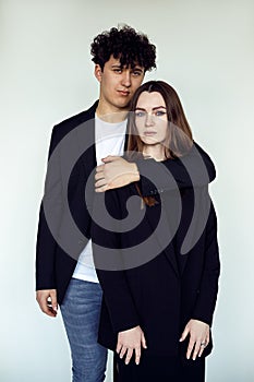Vertical portrait of young attractive brown-haired man and woman in black clothes stand together, embracing. White view