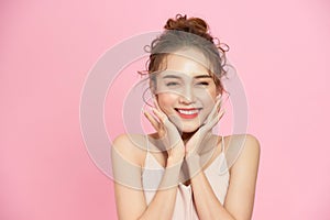 Vertical portrait of young beautiful smiling woman with naturally glowing skin, touching chin, isolated on pink background