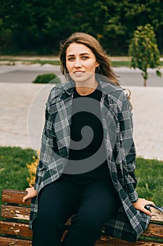 Vertical portrait of a young blonde woman sitting on a bench in a coat.