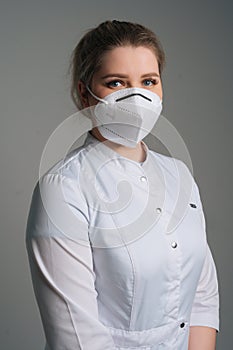 Vertical portrait of young female doctor wearing medical coat and protective face mask standing on dark isolated