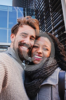 Vertical portrait of young multiracial couple. Man and woman tourist taking a selfie and smiling to the camera