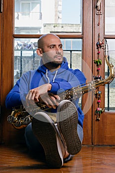 vertical portrait of young saxophonist sitting sleepily at home with his saxophone photo