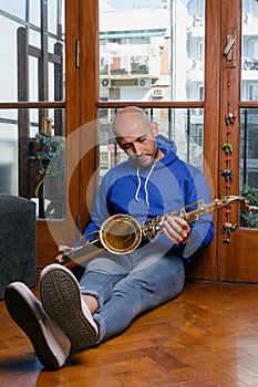 vertical portrait of young venezuelan sitting on the floor looking at his saxophone