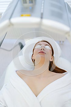 Vertical portrait of young woman having LED light facial photodynamic therapy treatment. Female patient wearing photo