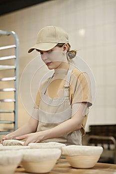 Young woman making fresh bread in bakery and kneading dough