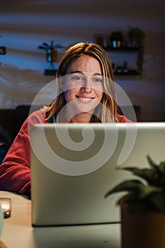 Vertical portrait of young woman working on her startup with laptop at home office sitting on desk at night. Happy