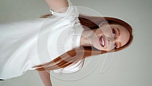 Vertical POV portrait of cheerful young woman talking via video chat using mobile phone looking at camera, on white