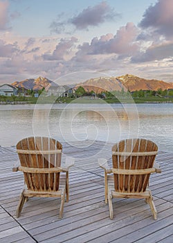 Vertical Puffy clouds at sunset Four wooden lounge chairs facing the reflective Oquirrh Lake at