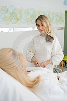Vertical rear view of unrecognizable young woman having consultation with female beautician therapist lying on couch