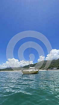 Vertical recreational sailing boat on ocean with mountain, blue sky and clouds in Hong Kong