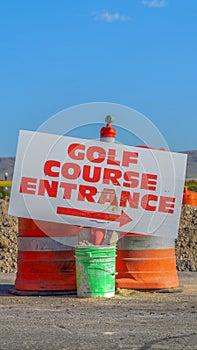 Vertical Road under construction with golf course entrance sign and traffic barrels