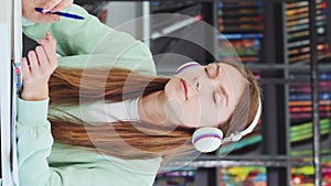 Vertical Screen: Caucasian schoolgirl wearing headphones daydreaming in library