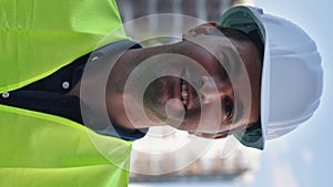 Vertical Screen: Smiling contractor in hard hat against multistory buildings