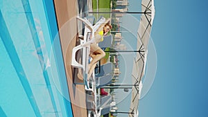 Vertical screen: woman in yellow bikini relaxing on poolside beach lounger