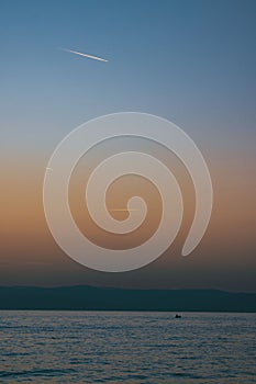 Vertical of seascape view at sunset with a boat swimming in water, a purple and misty sky background