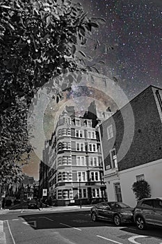 Vertical selective color of a night sky full of stars with buildings and cars in the foreground
