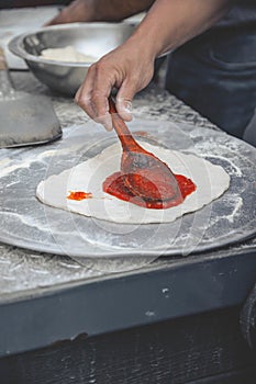 Vertical selective focus shot of a hand saucing the dough of pizza with a wooden spoon