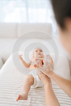 Vertical selective focus shot of unrecognizable female therapist doctor doing gymnastics and foot massage to adorable