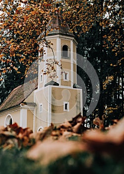 Vertical selective focus of a small chapel surrounded by colorful autumn trees in a forest