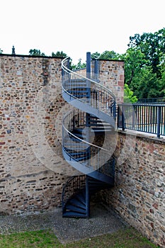 Vertical shoot of spiral stairs near a stone building with green trees in the background