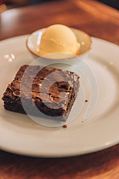 Vertical shot of an appetizing brownie with a scoop of ice cream on a round plate