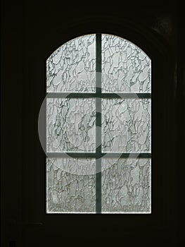 Vertical shot of an arch-shaped glass window on a dark background