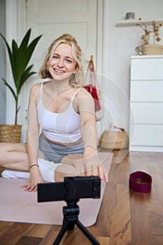 Vertical shot of athletic, fitness woman recording video of herself on digital camera, creating content for social media