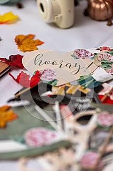 Vertical shot of autumn leaves, pieces of paper and a hooray heart sign on a table