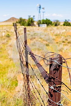 Vertical shot of a barbed-wire fence protecting a dry area with an old windmill in South Africa