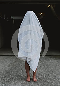 Vertical shot of a barefoot person wearing white ghost sheet.Spooky concept