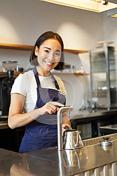 Vertical shot of barista, girl in coffee shop, pouring water in kettle, preparing order in cafe, smiling at camera