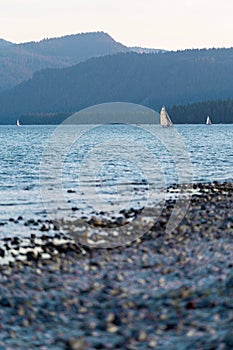 Vertical shot from the beach of sailboats sailing in the ocean and mountain in the background